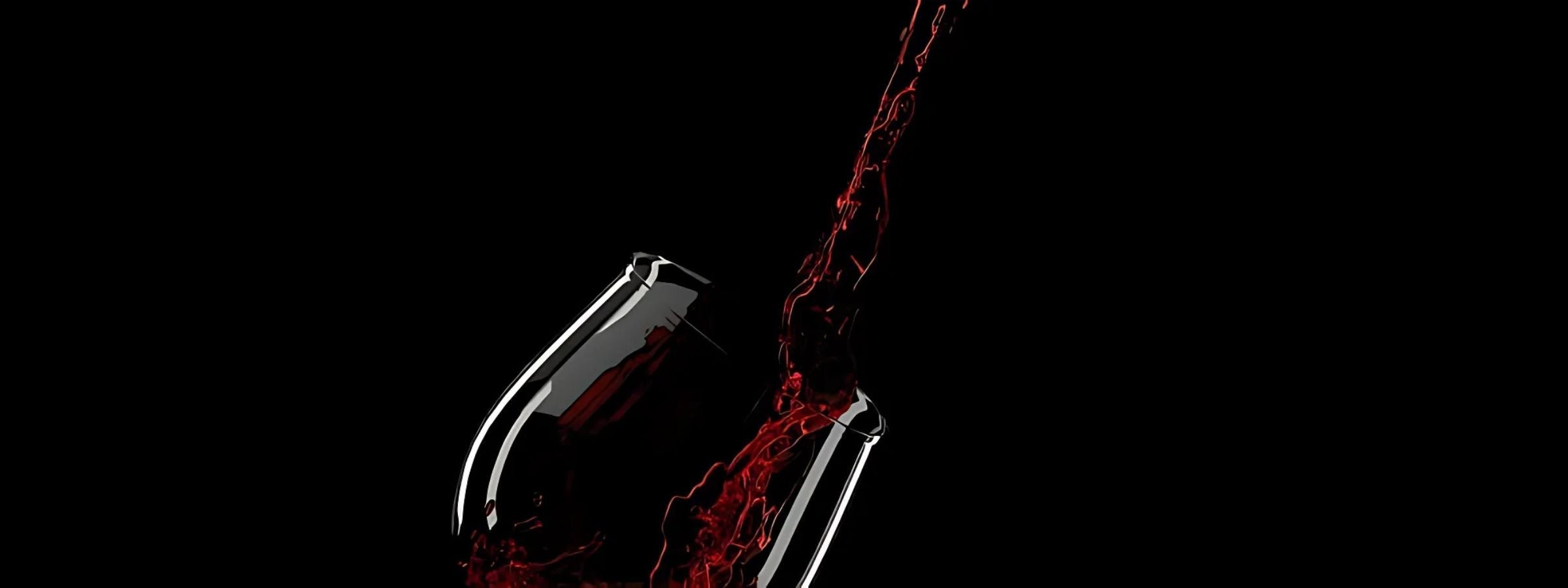 Assorted red wine bottles and glasses on a rustic table with grapes, cheese, and candlelight