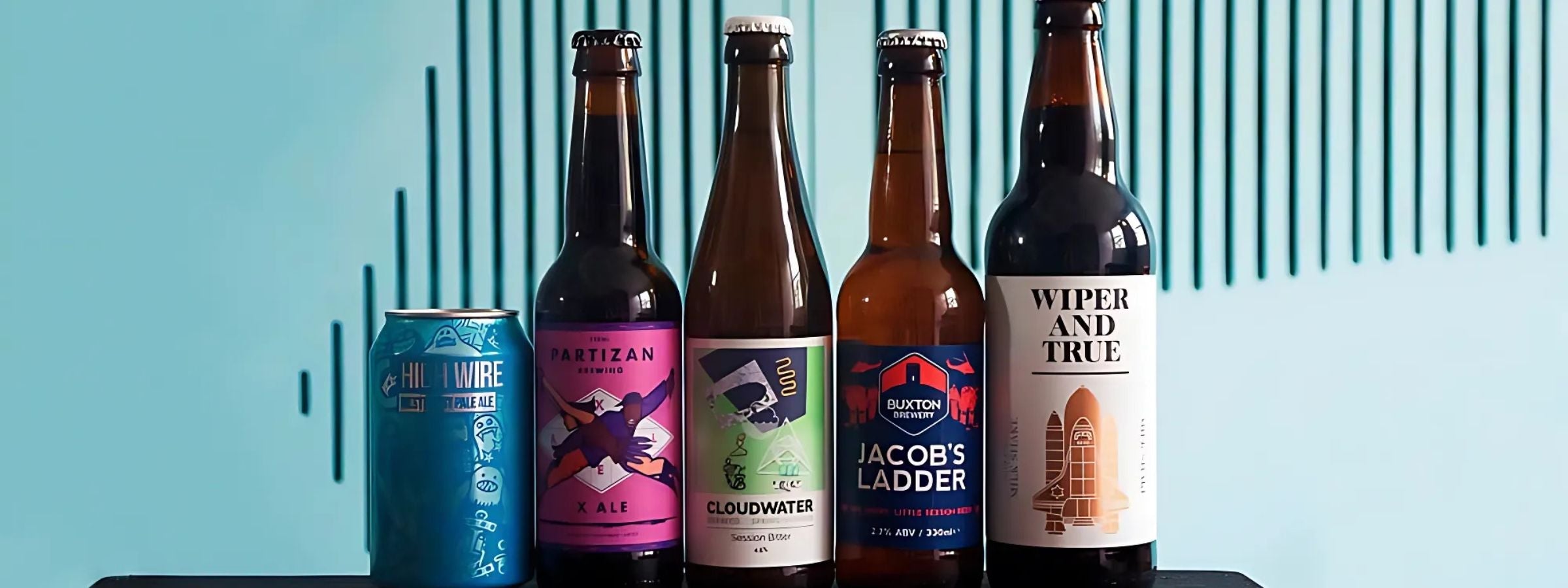 Cans and bottles of craft beer in mixed styles on a wooden table with hops and branded glassware