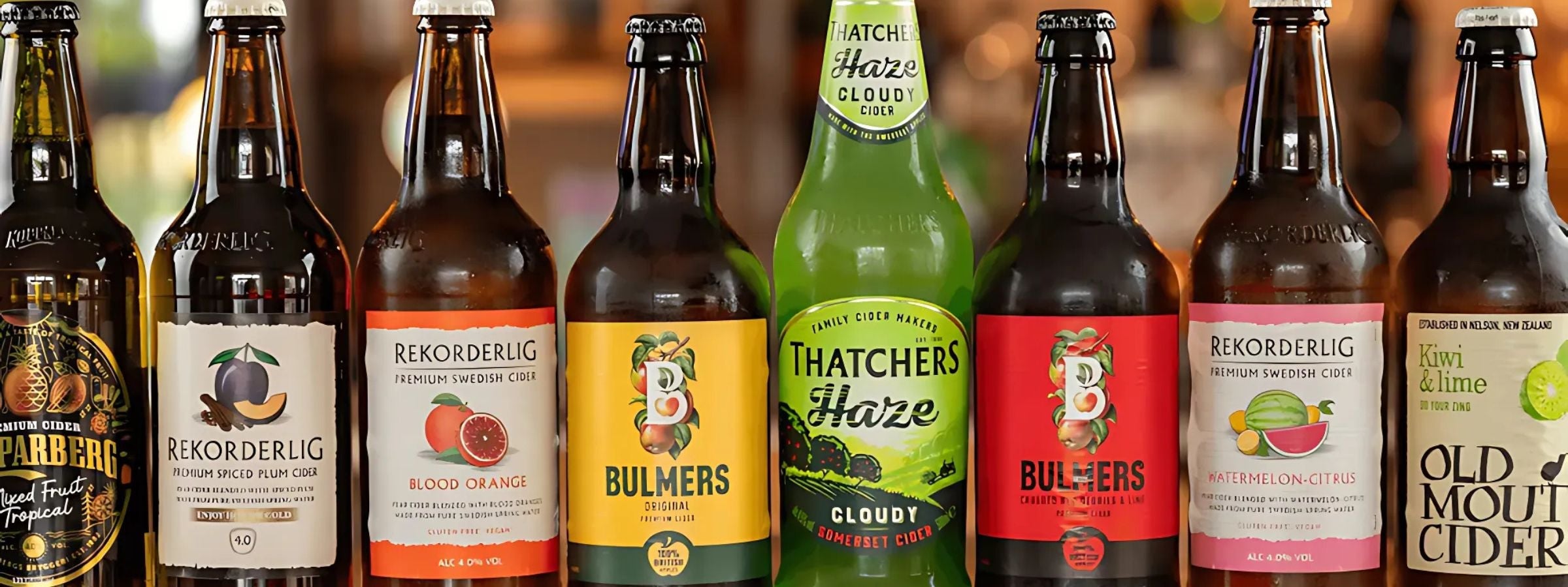 Bottles and cans of cider on an outdoor table with fresh apples, glasses, and summer setting