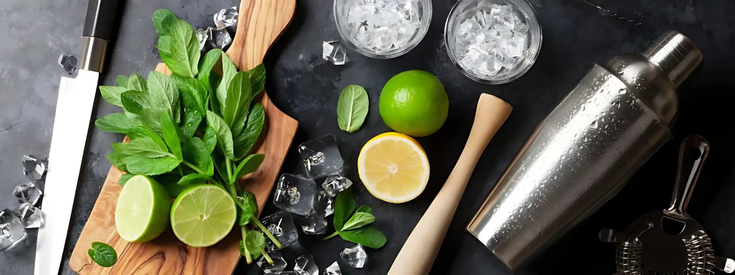 Cocktail syrups, mixers, garnishes and bar tools displayed around a cocktail shaker and glass setup