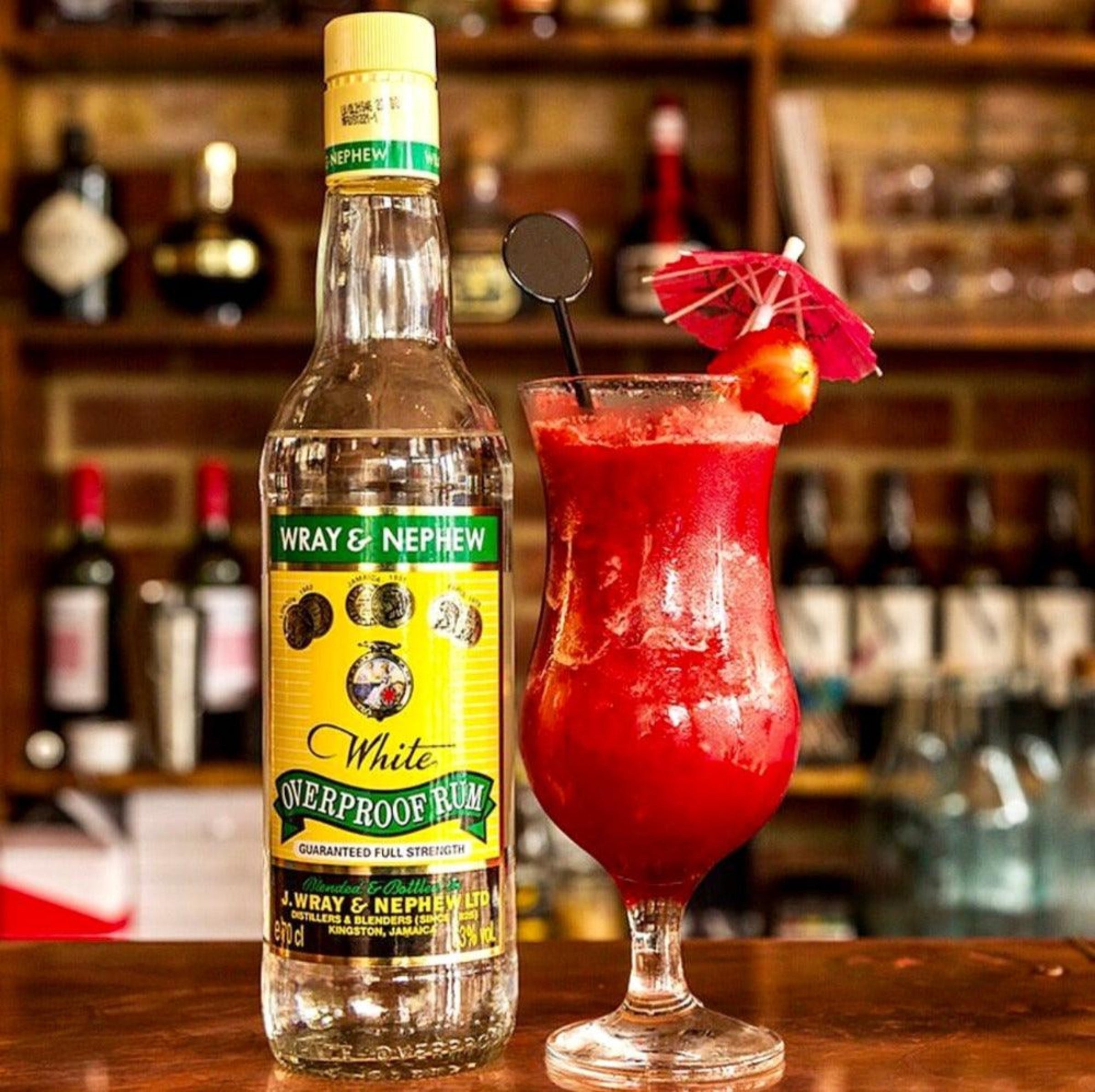 Wray & Nephew White Overproof Rum 70cl bottle with cocktail glass and lime garnish on rustic bar

